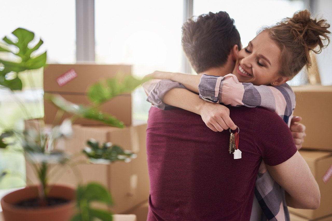Happy couple holding a key and moving boxes behind